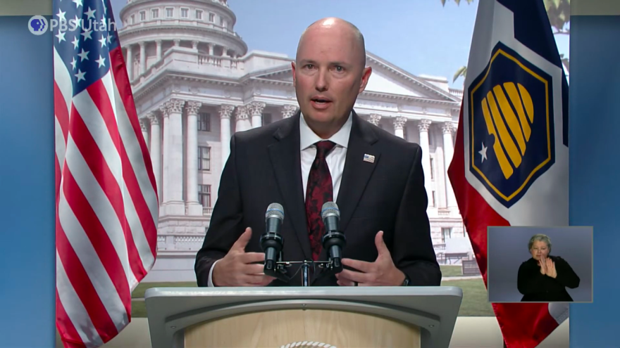 Governor Spencer Cox speaks behind a podium backed by the American and Utah state flags. 