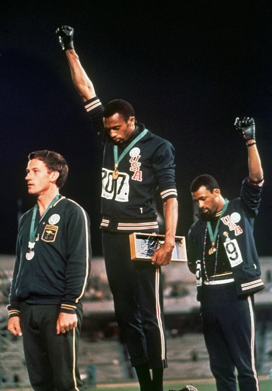 FILE - In this Oct. 16, 1968 file photo, extending gloved hands skyward in a Black power salute as a form of racial protest, U.S. athletes Tommie Smith, center, and John Carlos stare downward during the playing of national anthem. 