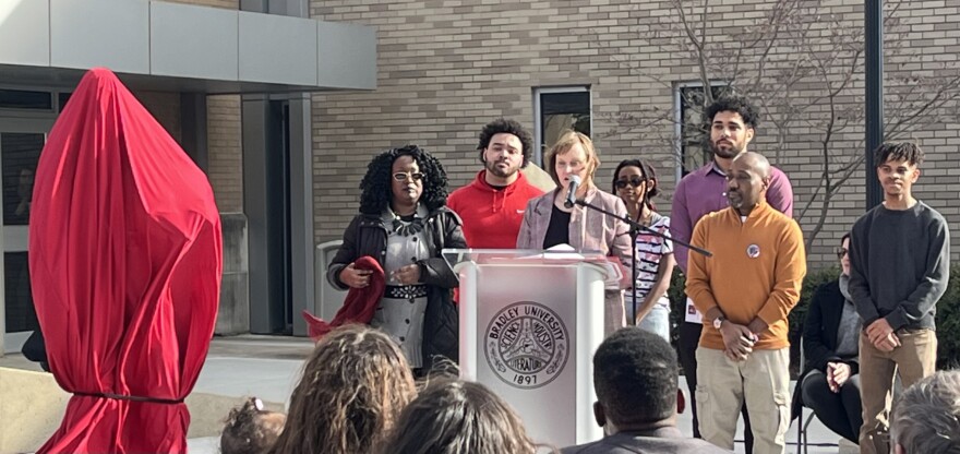 Dr. Michelle Fry, Department Chair and Associate Professor of Chemistry at Bradley University (center, at podium) reads from Major Robert H. Lawrence, Jr.'s doctoral dissertation at the unveiling of his statue on Bradley campus. She's surrounded by current and former recipients of a scholarship named after Lawrence.