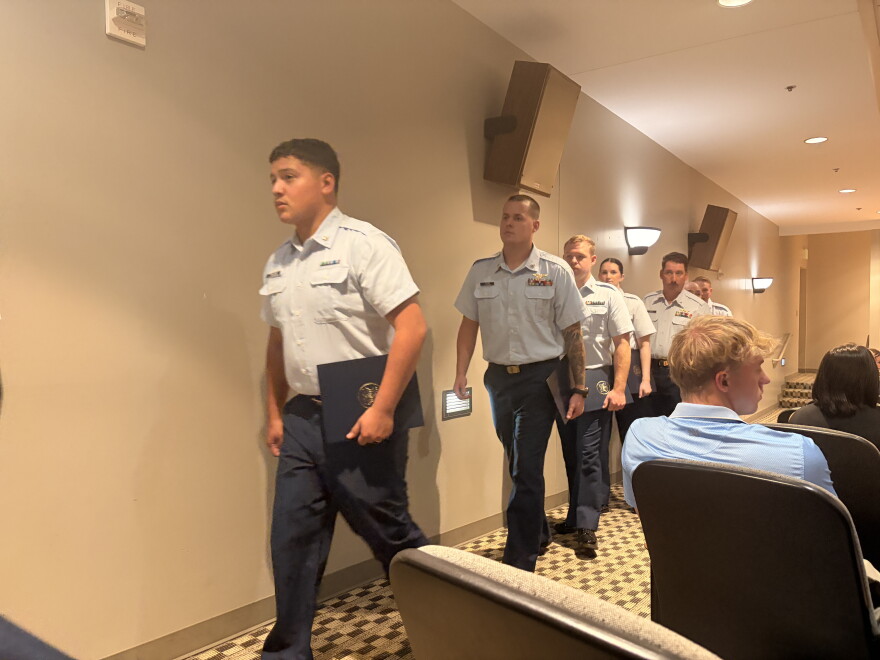 Coast Guard graduates walk along the outside aisle of an auditorium.