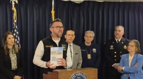 Aidan O'Connor with New York State Volunteer Ambulance and Rescue Association, flanked by state legislators, holds up a report on challenges with the rural EMS system in New York state during a news conference on Wednesday, March 11, 2026 in Albany.