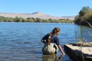 A woman wears waders as she stands in a lake near mountains.