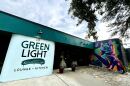 Exterior of a building says Green Light Lounge + Kitchen on a white wall with a mural of a purple cat to the right