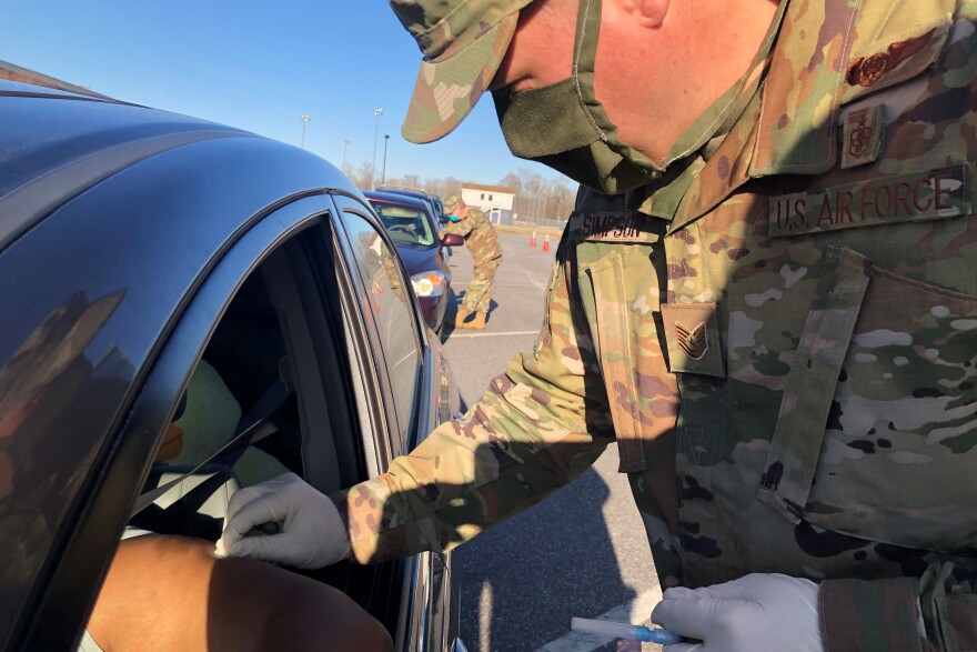 At a drive-through vaccination site in Elizabeth City, N.C., Tech Sgt. Steven Simpson of the North Carolina National Guard administers a COVID-19 vaccination as Maj. Hollis Guenther gives the next recipient instructions about the vaccine.