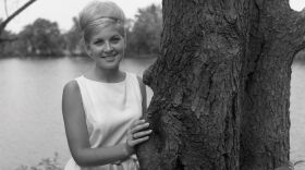 A photo of young Charlotte Thompson Suhler in the 1960s by a tree in front of a lake.