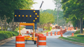 Lights on a construction sign direct drivers around orange barriers during a road project. 