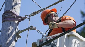 FILE - In this Wednesday, Aug. 4, 2021, file photo, Travis Sheetz, a worker with the Mason County (Wash.) Public Utility District, installs fiber optic cable on a utility pole, while working with a team to bring broadband internet service to homes in a rural area surrounding Lake Christine near Belfair, Wash.