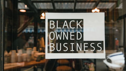 Black owned business sign taped on a window, seen from outside a store.
