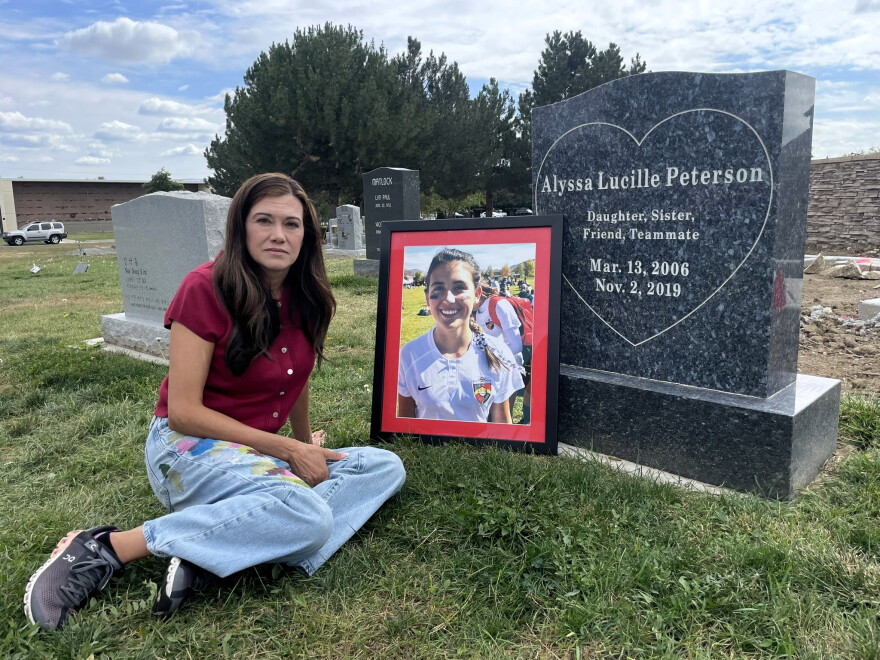 Stella Deslongchamp sits beside a photograph of her daughter, Alyssa Peterson, at Alyssa’s gravesite in Wheat Ridge on Sept. 29, 2026. Alyssa died by suicide in 2019. She was 13.