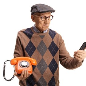 Elderly man holding an old vintage rotary phone and a smartphone.