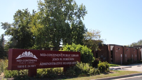 A brown sign sits among bushes and flowers. It reads "Mid-Continent Public Library John W. Ferguson Administrative Headquarters"