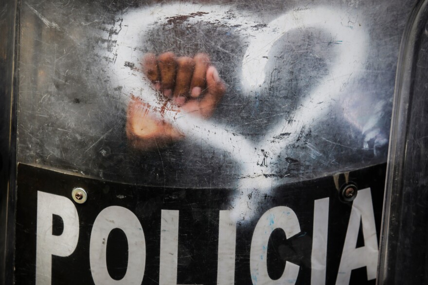 With heart-shaped graffiti spray-painted by activists on a shield, Nicaraguan riot police stand by in August 2019 as anti-government protesters in Managua call for the reinstatement of health workers who lost their jobs for assisting protesters during a deadly 2018 uprising against President Daniel Ortega.