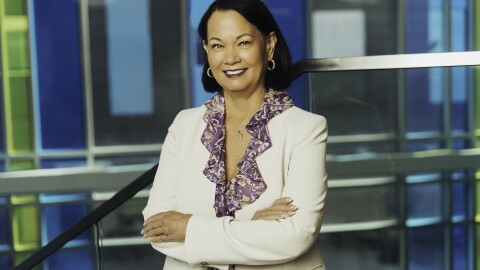 Ebert is standing with her arms crossed, smiling and wearing a purple shirt and a white jacket. 