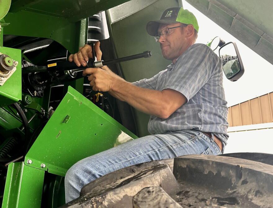 Farmer sits on a tire working on a combine.