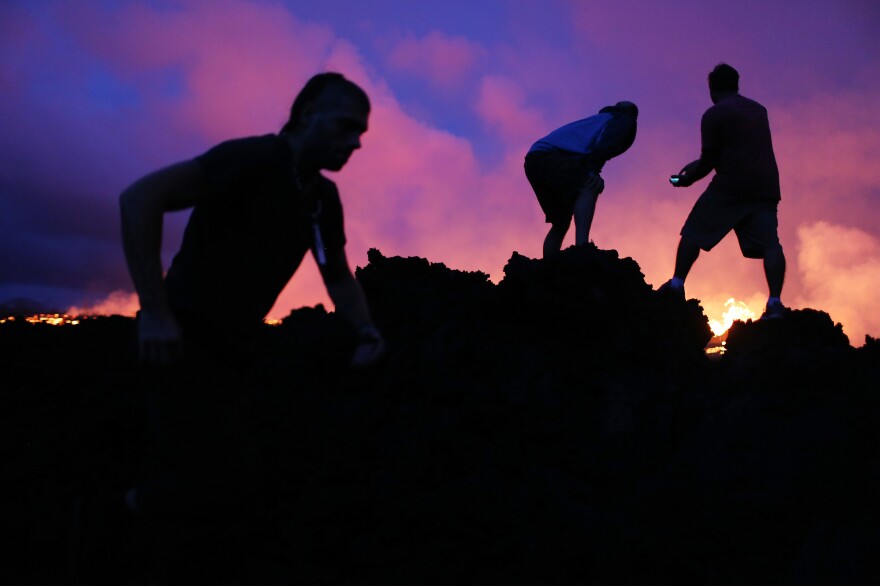 Onlookers gather on newly hardened lava to catch a view as lava erupts and flows in the distance. Tama says people view the lava with "a mixture of fear and curiosity."