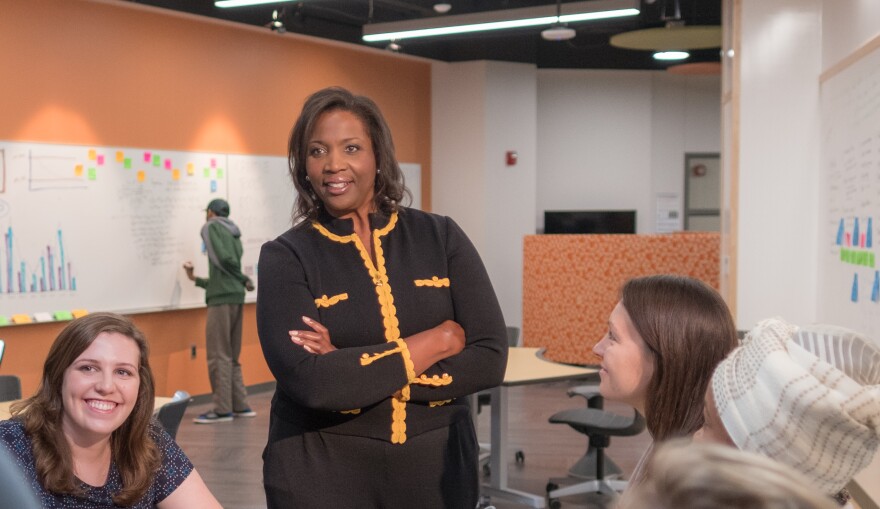 Lisa Cook stands in a black blazer with yellow trim, smiling with her arms crossed in front of four young women students 