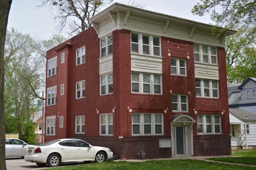 Exterior view of a brick, three-story building with white trim. Two cars can be seen parked at left.
