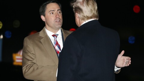 frank larose, in a camel jacket, white tie and red, white and blue plaid patterned tie greets donald trump, seen from behind, in a black coat