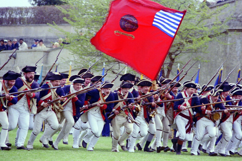 Troops wearing the Revolutionary War uniforms of the 9th Virginia Regiment, Corps of the Continental Line, participate in a drill and firing demonstration during the Cessation of Hostilities Bicentennial Celebration at the Pentagon River Plaza. The flag of the ceremonial 2nd Pennsylvania Regiment, Corps of the Continental Line, is carried in the background.