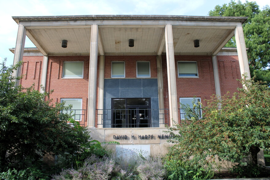 A two-story red brick building with large columns and square windows, surrounded by trees and shrubs. The sign above the entrance reads “David H. Harts Memorial.”.