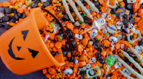 Orange pumpkin pail spilling Halloween candy on black stone surface with skeleton hands grabbing candy