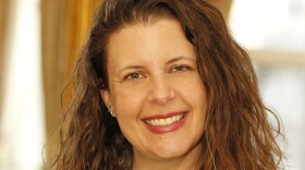 A smiling woman with curly brown hair, wearing a green blouse and a silver necklace