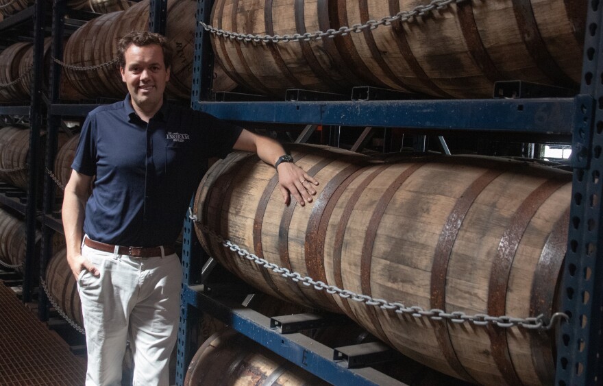 A man leans against rows of barrels filled with bourbon and whiskey.