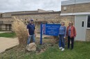 Chris Hagerman, Susan Hagerman and Michelle Allen standing next to a sign with the James Couzens Auditorium and Bath School Museum, in front of the Bath School Museum entrance