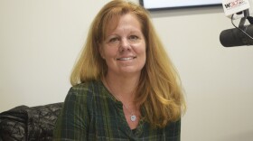 Woman in green patterned top seated in a studio next to a microphone 