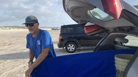Former plastics engineer Neil McQueen pulls his board out to surf the waves off Mustang Island in Texas. Neil now fights against plastic pollution plaguing Texas' beaches and coastal waters.
