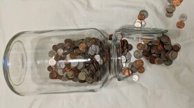A glass jar lying on its side with coins coming out of it.