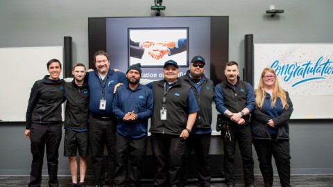 A group of eight people in uniform pose in front of a "congratulations" sign