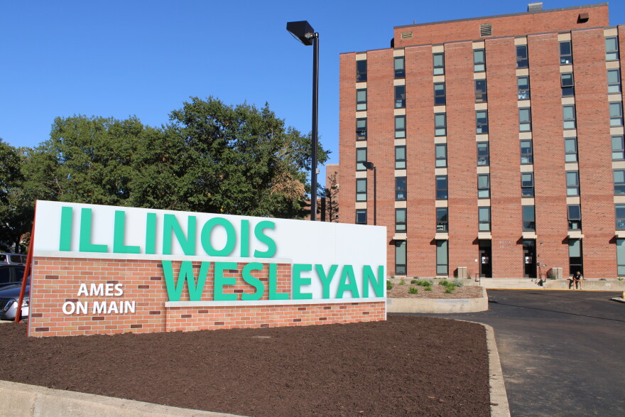 A brick sign for Illinois Wesleyan Ames on Main in front of a tall brick building.