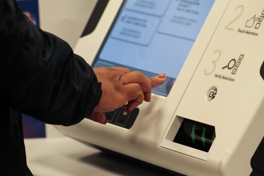 A person's hand presses a button on an electronic voting machine.