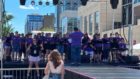 Performers stand and sing on a stage outdoors.