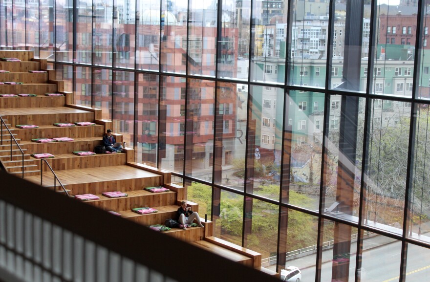 Convention center guests sit working next to floor-to-ceiling windows that show off views of downtown Seattle.