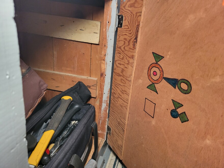 Inside a cabinet, a tool bag within and a series of colorful shapes drawn on the inside of the door