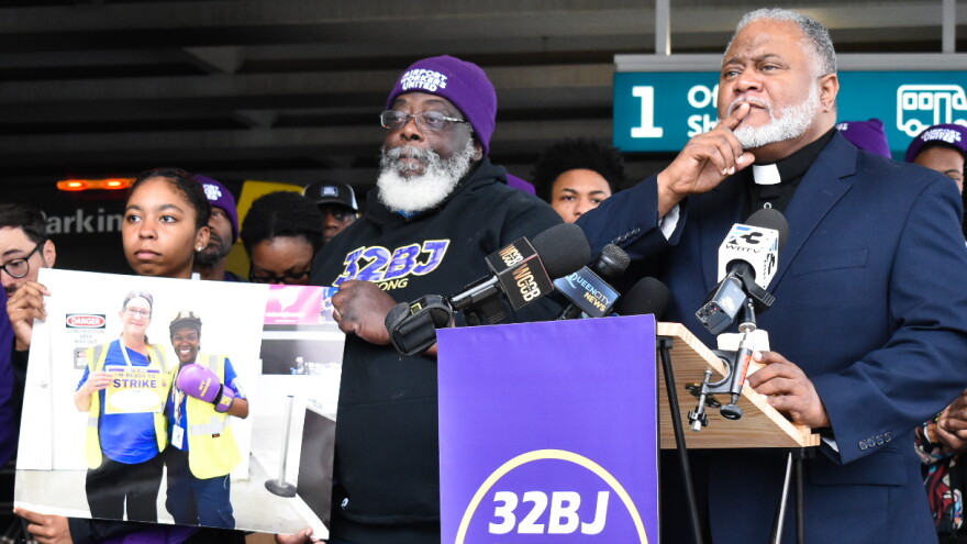 Two men and one woman behind lectern, woman holds sign