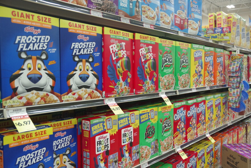A grocery store shelf is filled with different Kellogg brand cereal boxes, each with their own colorful cartoon mascot.