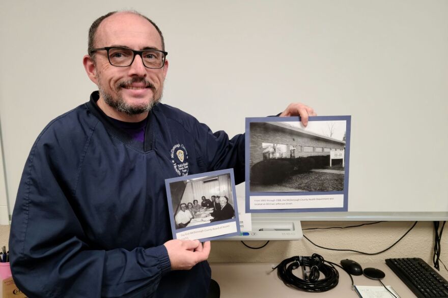Chris Adams with photos of the first McDonough County Board of Health in 1975, and the health department’s building on East Jefferson Street during the 1980s.