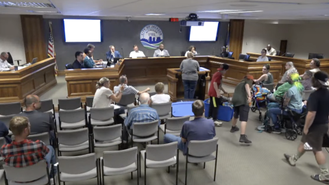 People walk down the aisle at a city council meeting