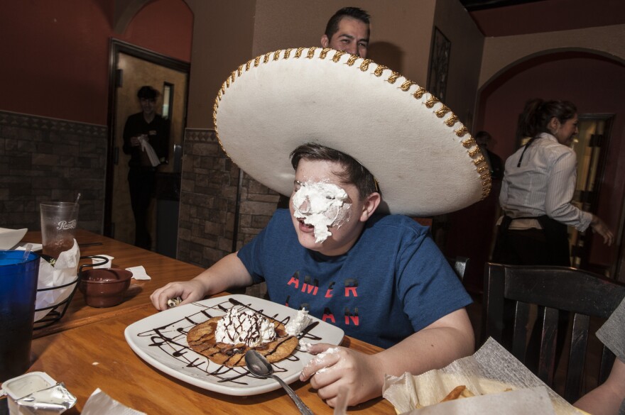 A white boy at a Mexican restaurant in a sombrero with frosting on his face.