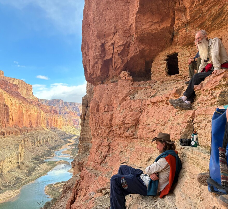 Two people sit along the wall of the Grand Canyon.