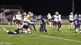 A football running back is swarmed by a bunch of defenders. 