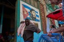 A man carries a pig at the entrance of a market, decorated with a mural of Fidel Castro, in Havana, Cuba, Wednesday, Aug. 12, 2026.