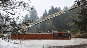 Only the top part of a firetruck is visible as it is partially submerged in a flooded river. 