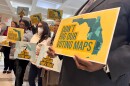 People hold up signs that read "Don't Rig Our Voting Maps" and "Partisan Power Grab" 