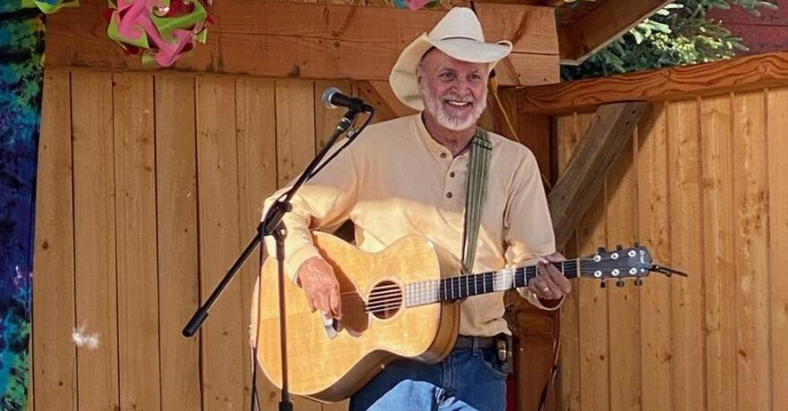 A white man in a cowoby hat playing an acoustic guitar