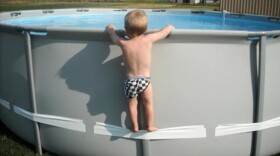 a very young child climbs onto a vinyl rail of an above ground pool