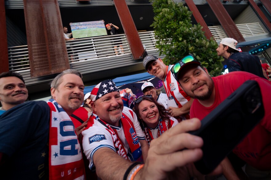 American Outlaws St. Louis Chapter president Kevin Marshall, second from left, takes a selfie alongside club members and St. Louisans who set their TV up for hundreds to watch after a power outage cut the USMNT vs. Paraguay stream outside Amsterdam Tavern on Friday, June 12, 2026, in south St. Louis.